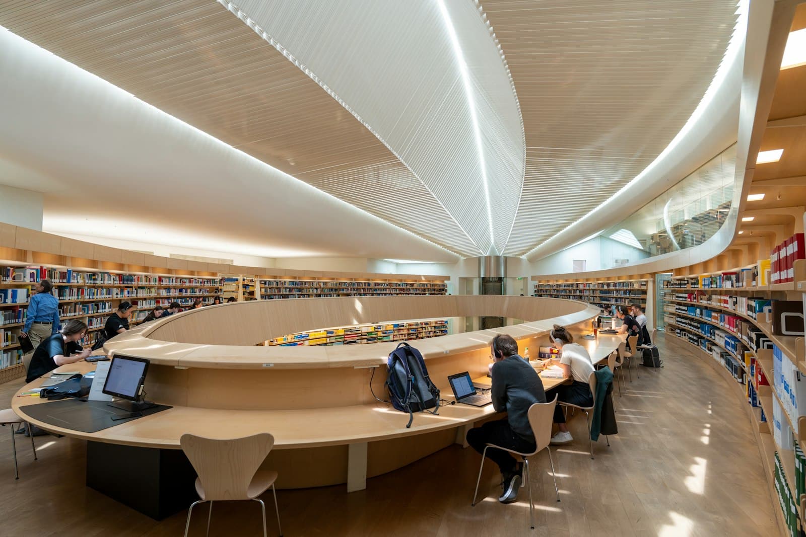 Students working at curved tables in a bright modern university library